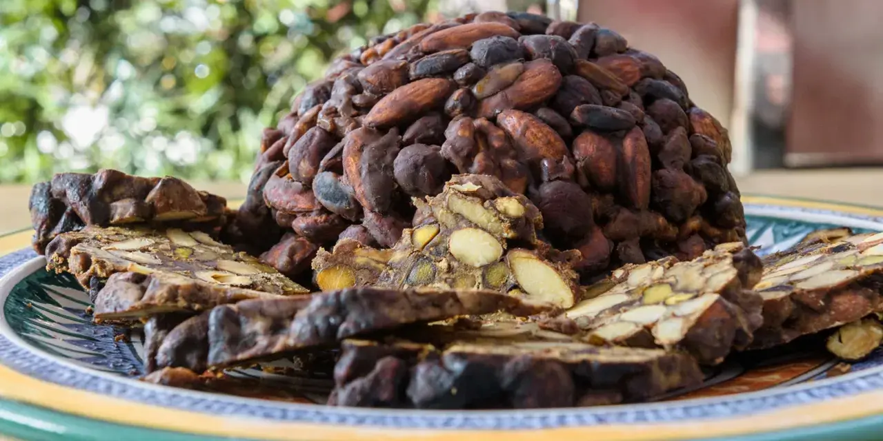 Un pan pepato a forma di cupola, ricoperto di mandorle e cacao, con fette tagliate che rivelano frutta secca e spezie.