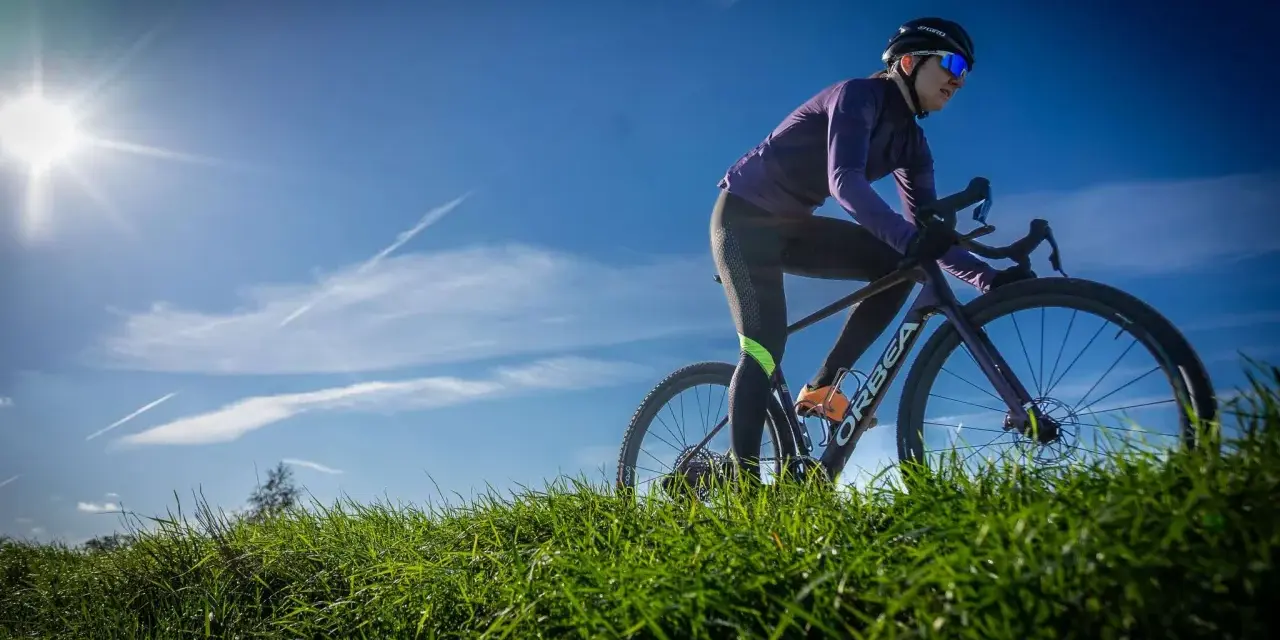 Kobieta na rowerze gravelowym, w kasku i okularach, pokonuje pagórkowaty teren. Różne rodzaje treningów kolarskich pozwalają na wszechstronny rozwój.