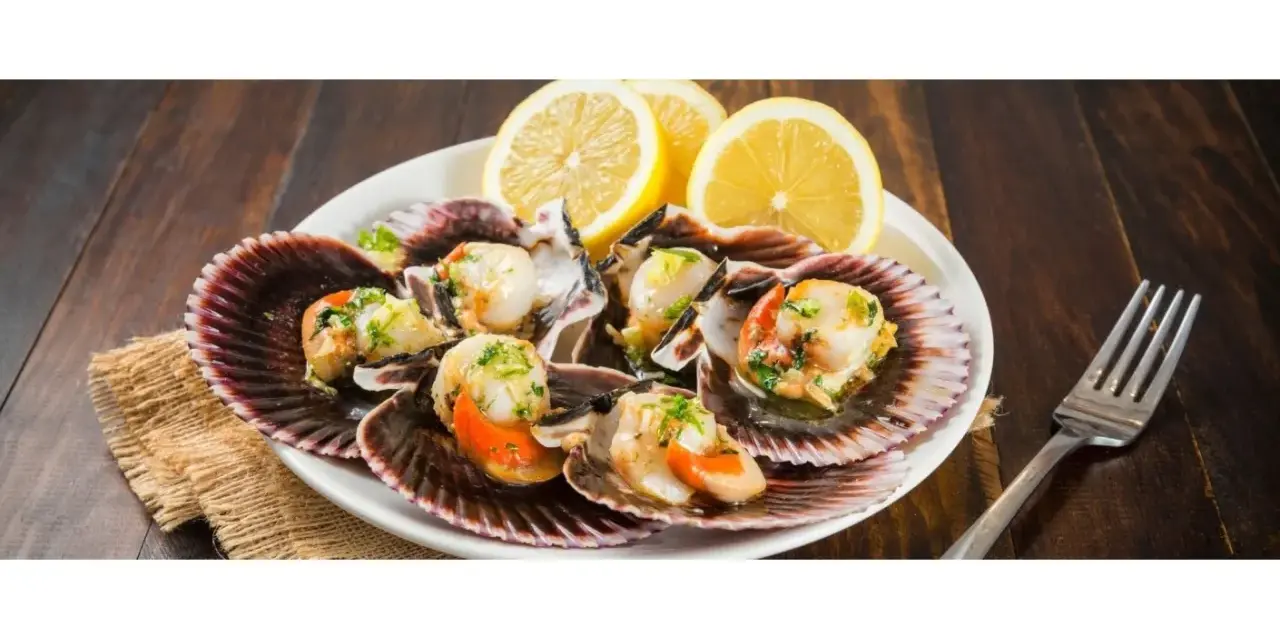Zamburiñas a la plancha servidas en sus conchas, adornadas con perejil picado y rodajas de limón. Un plato delicioso y fresco.