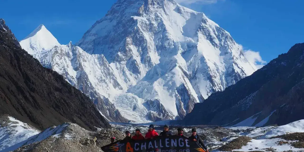 Grupa ludzi z banerem przed majestatycznym szczytem K2 w Karakorum. To wyzwanie w górach Pakistanu.