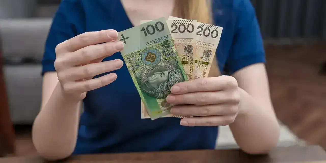 Dłonie trzymają polskie banknoty: 100 zł i dwa razy po 200 zł. To może być część zasiłku rodzicielskiego.