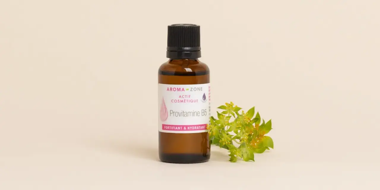 Flacone di Provitamina B5, un attivo cosmetico fortificante e idratante per la pelle, accanto a un rametto fiorito.