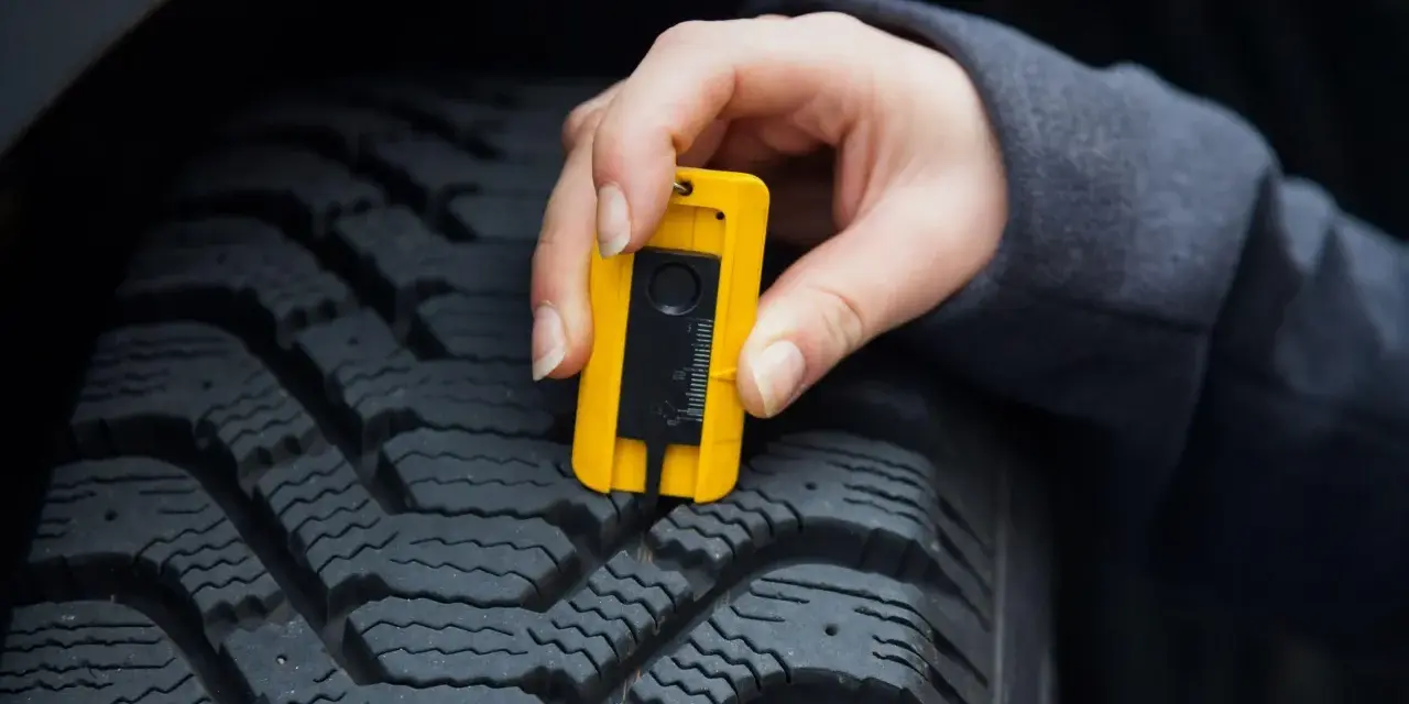 Misurazione del battistrada di uno pneumatico con un calibro giallo. La **sigla TWI** indica il limite di usura.