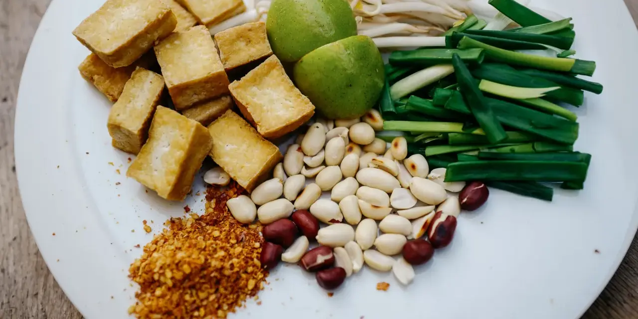 Składniki do pad ka prow: smażone kostki tofu, kiełki fasoli mung, szczypiorek, orzeszki ziemne, limonka i płatki chili.