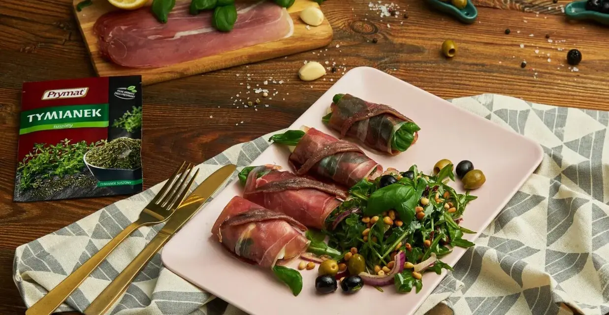 Roladki z szynką parmeńską, ziół, anchois i serka, podane z sałatką z rukoli, oliwek i orzeszków pinii.