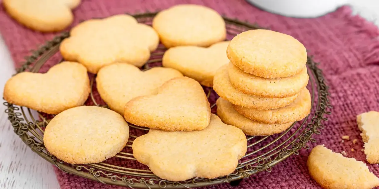 Deliziosi dolci da fare in casa, biscotti a forma di cuore e fiori su un vassoio di metallo, adagiati su un panno color prugna.