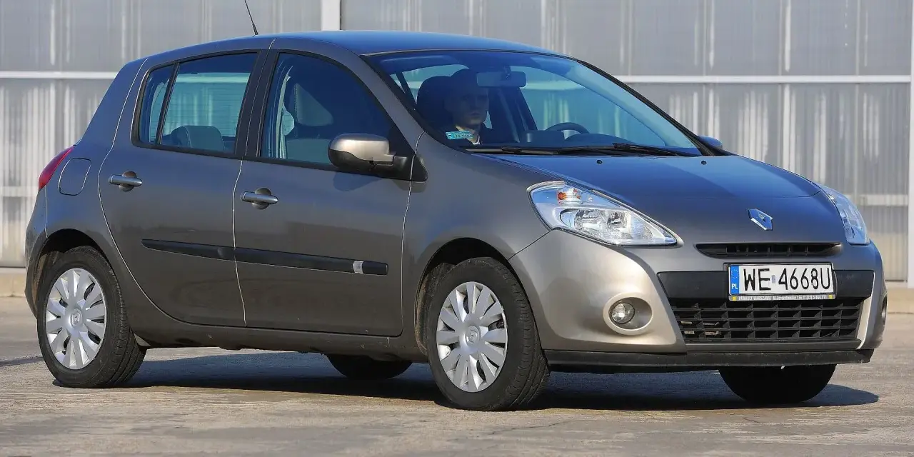 Szary Renault Clio 3 z kierowcą za kierownicą, zaparkowany na zewnątrz.