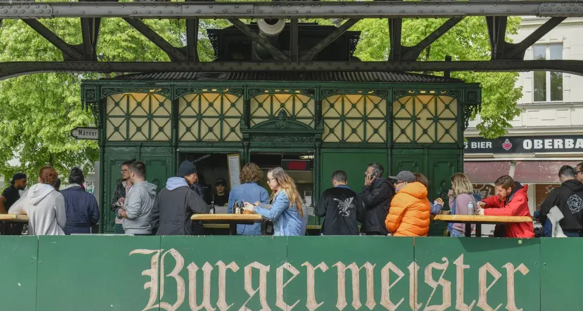 Menschen sitzen an Tischen vor dem Burgermeister in Berlin.