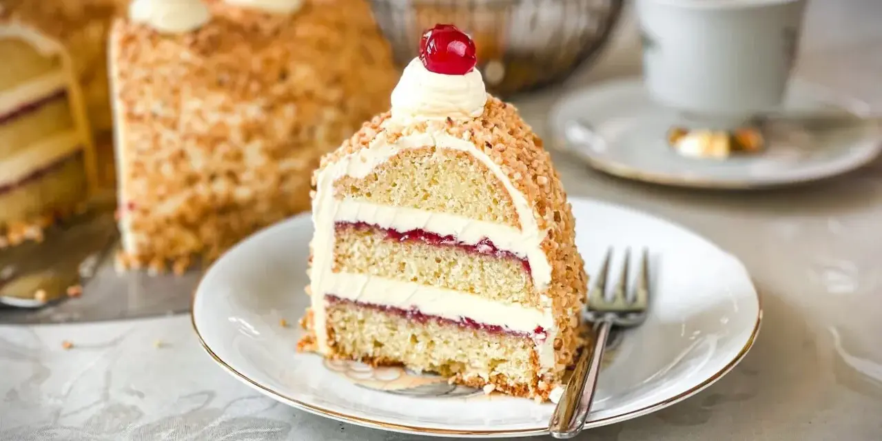 Ein Stück einer köstlichen Torte mit Buttercreme und roter Marmelade, umhüllt von gehackten Nüssen. Perfekt für die besten Torten Rezepte!