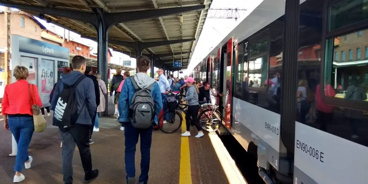 Ludzie czekają na pociąg na stacji w Lęborku. W tle widać budynek dworca i peron.