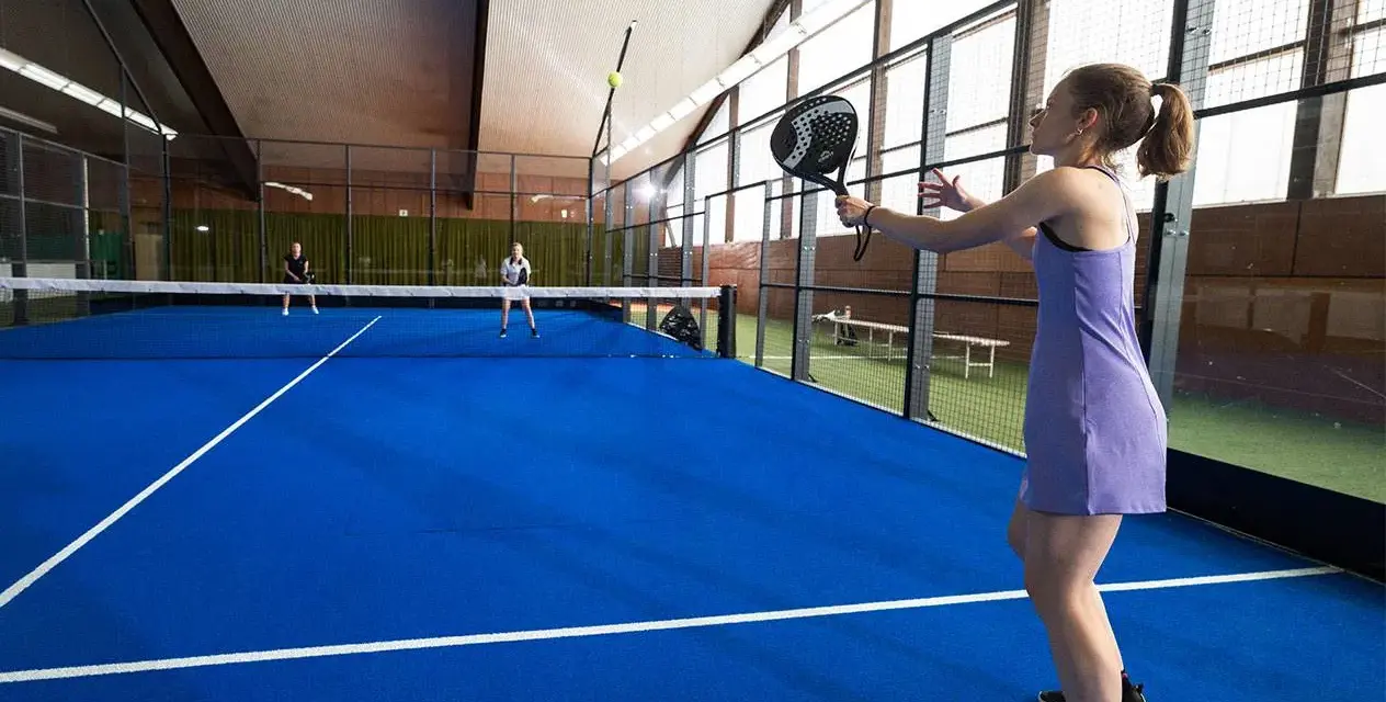 En kvinna i lila klänning spelar padel. Hon är redo att slå bollen på den blå banan.