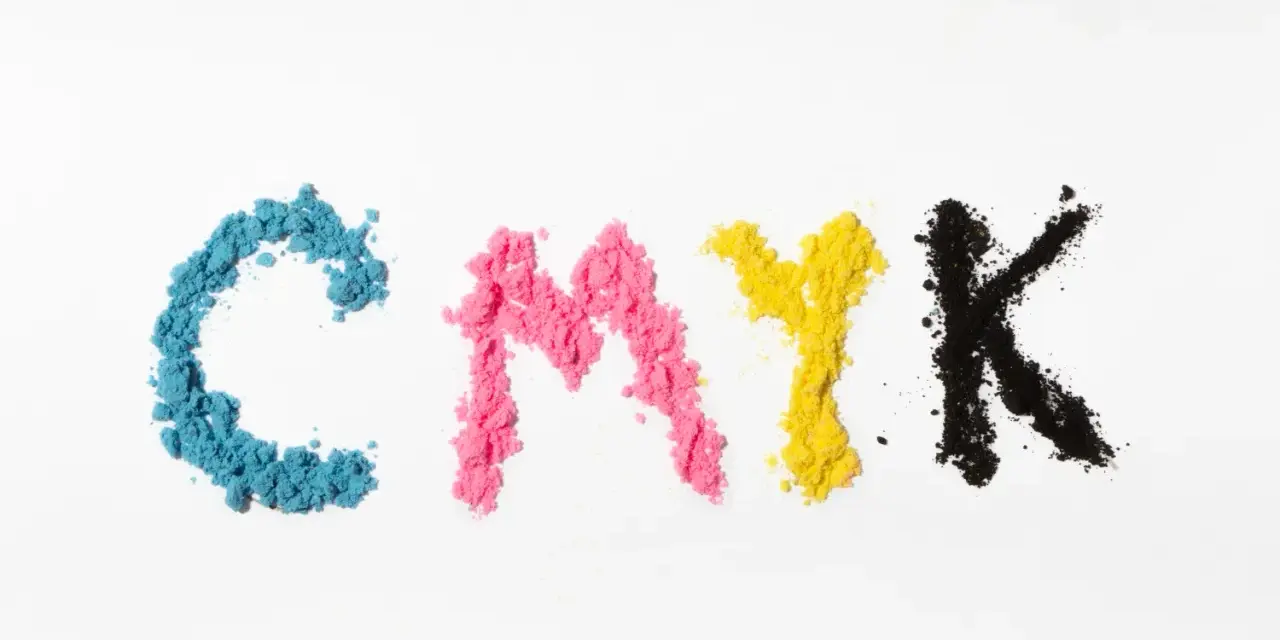 Litery CMYK ułożone z kolorowego proszku. Kolejność kolorów: cyjan, magenta, żółty, czarny.