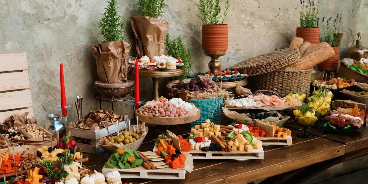 Stół z bogatym cateringiem: sery, wędliny, owoce, słodkości i pieczywo.