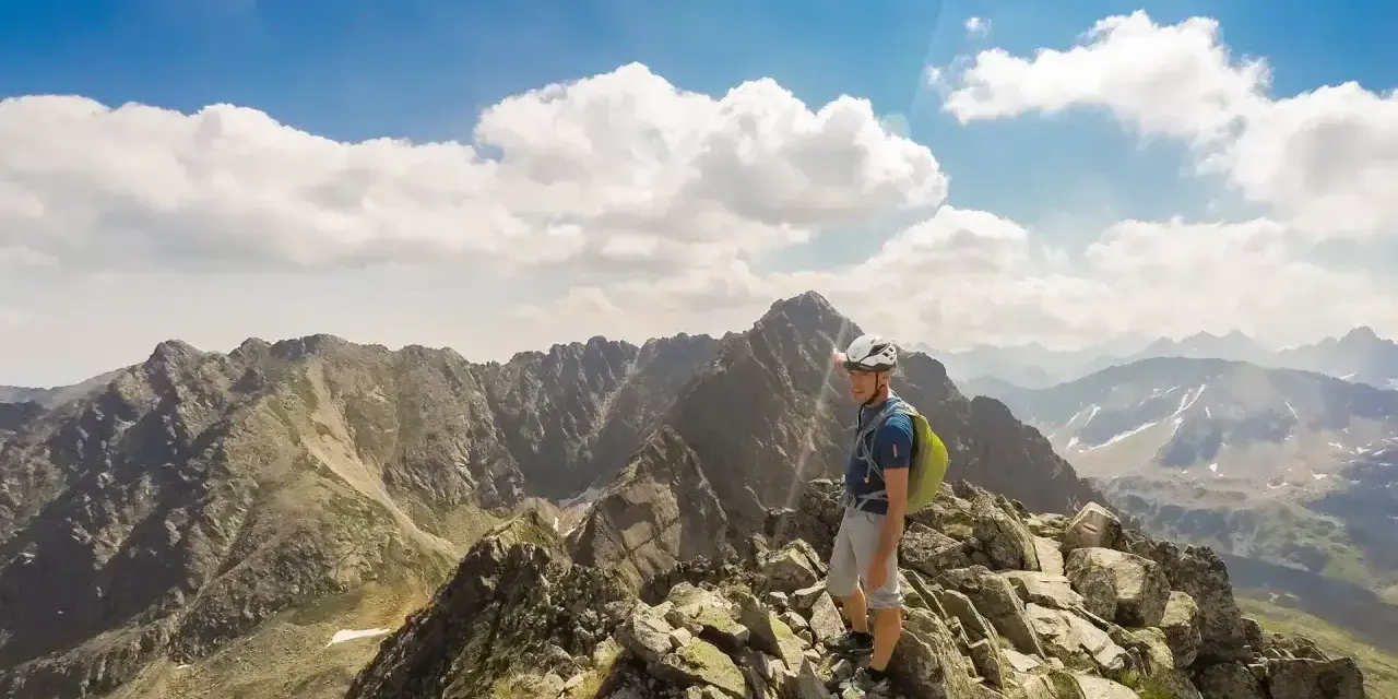 Turysta na skalistym szczycie, wskazujący drogę na Orlej Perci. W tle majestatyczne Tatry.