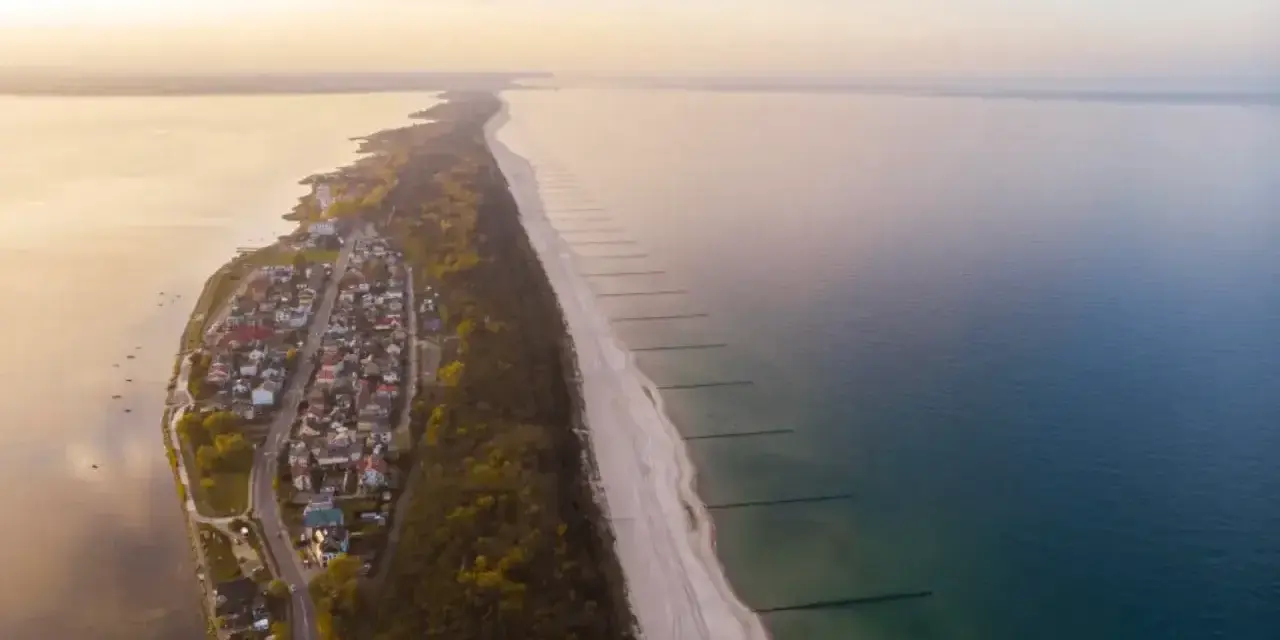 Widok z lotu ptaka na malownicze chałupy nad morzem, z piaszczystą plażą i spokojną wodą.