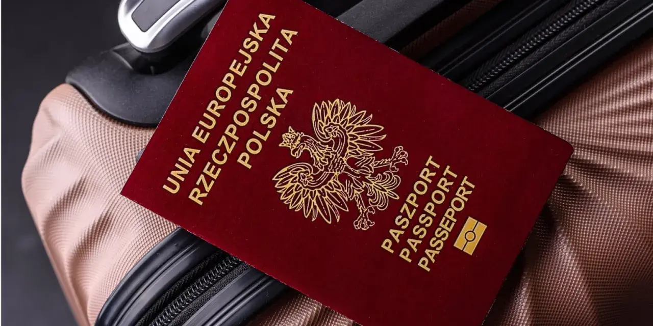 Czerwony paszport Polski z godłem orła leży na brązowej walizce.