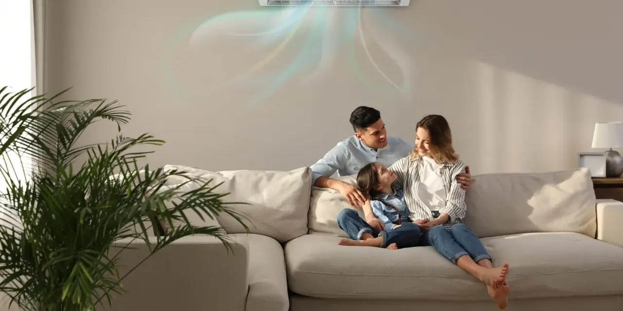 Famiglia felice sul divano, con l'aria condizionata che soffia aria fredda. Scopri come impostare condizionatore aria fredda per un comfort ottimale.