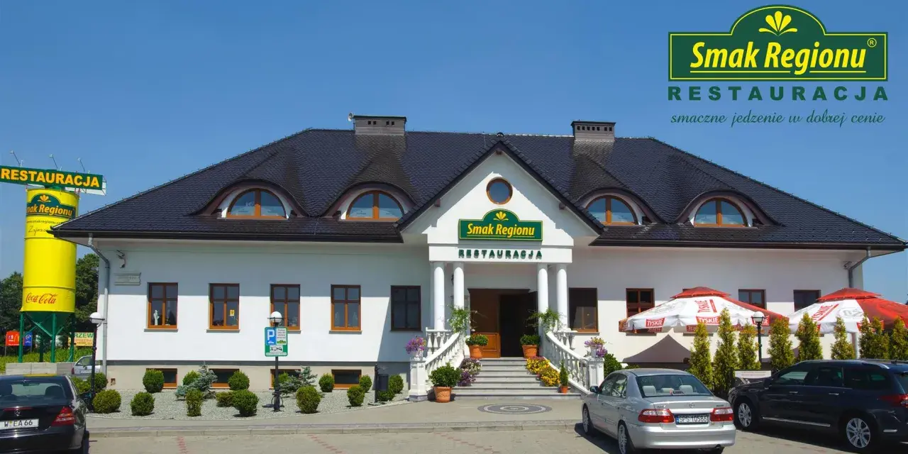 Restauracja "Smak Regionu" z białym budynkiem, schodami i samochodami na parkingu.