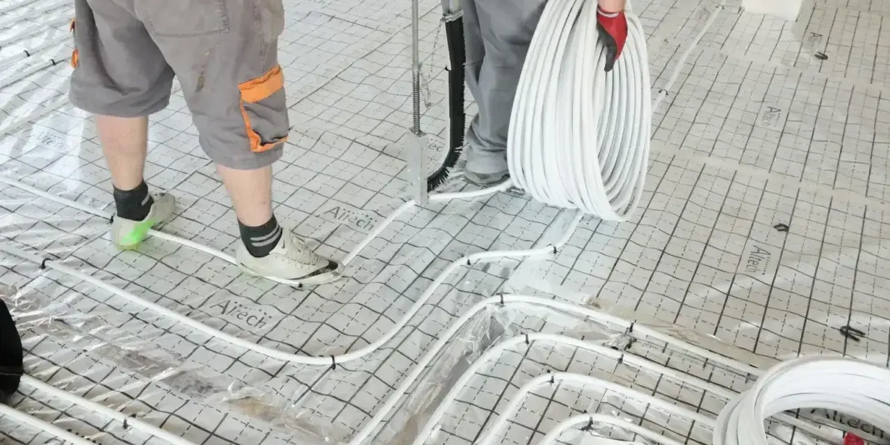 Pracownicy układają rury do ogrzewania podłogowego na siatce. Wkrótce powstanie tu szlichta, która zapewni komfort cieplny.