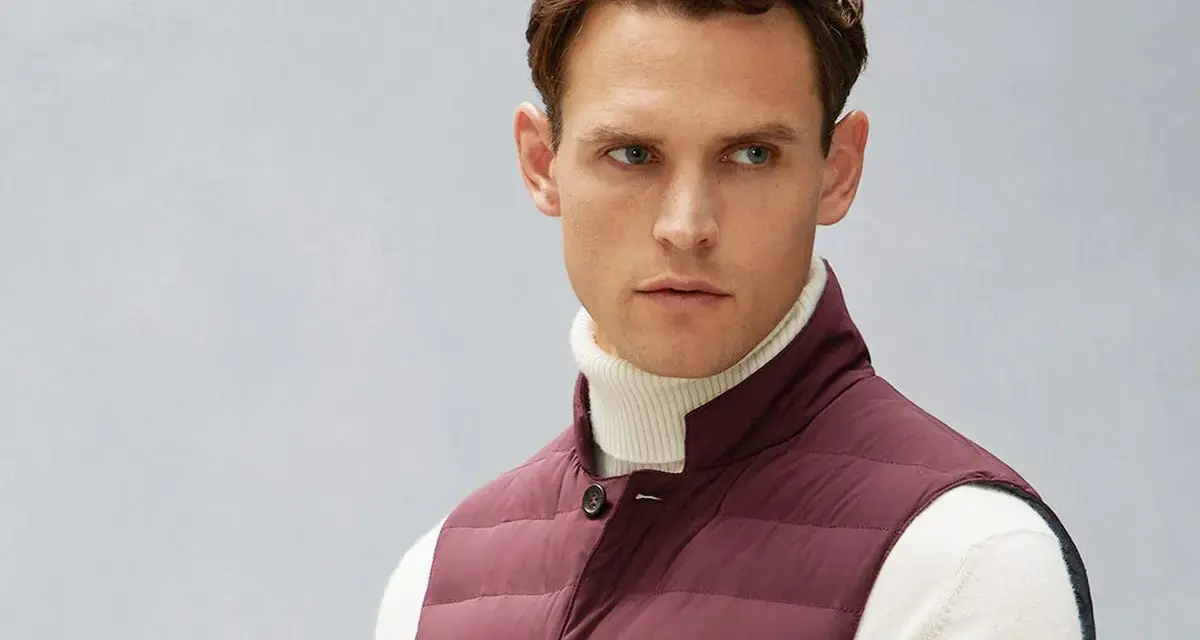 Uomo con gilet imbottito bordeaux sopra dolcevita bianco. Il gilet, un capo versatile, aggiunge stile e calore.