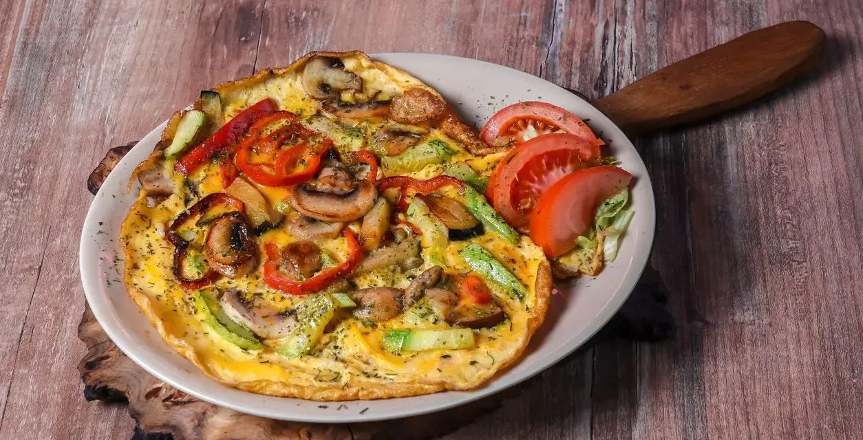 Pyszny omlet z pieczarkami, papryką i cukinią, udekorowany pomidorem i sałatą.
