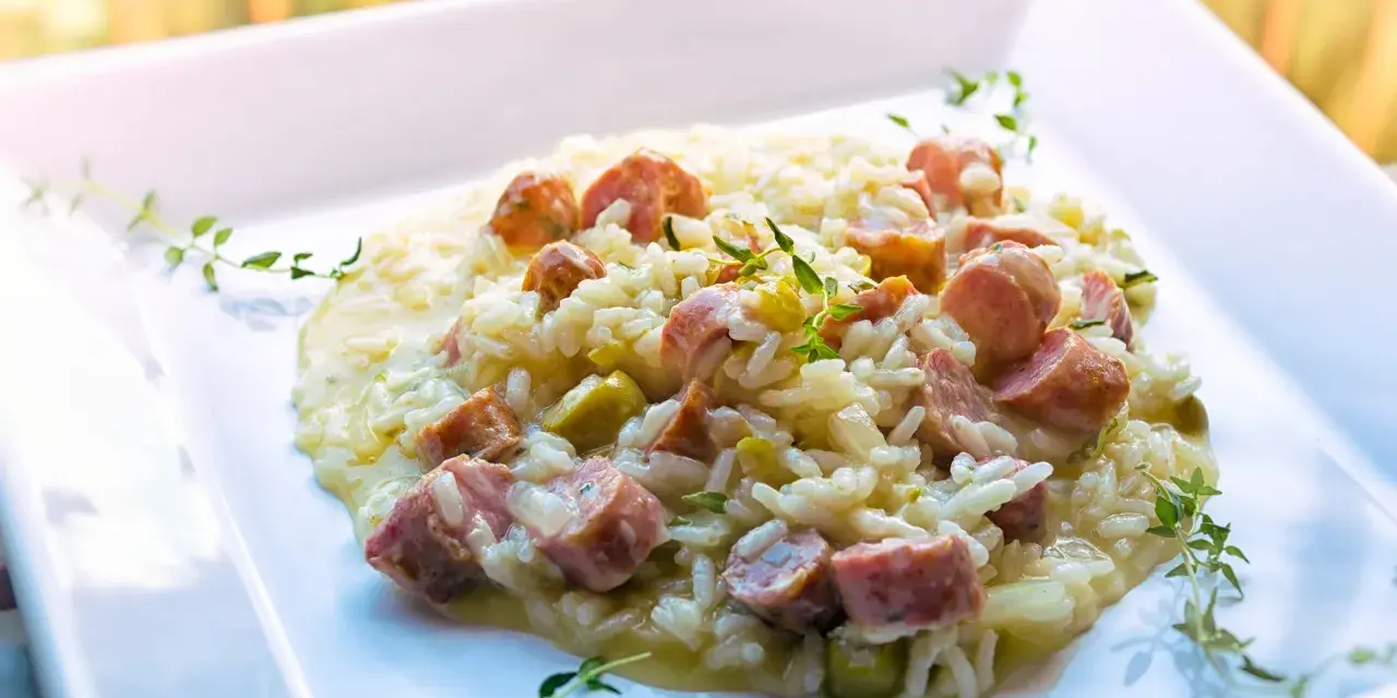 Un cremoso risotto con salsiccia, piselli e timo, servito su un piatto bianco.