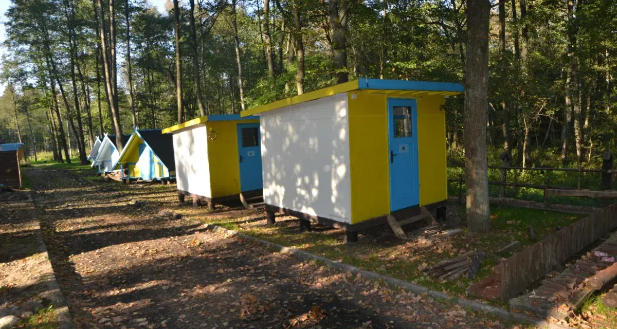 Kolorowe domki kempingowe w lesie, jak małe perły Krutyni, czekają na gości.