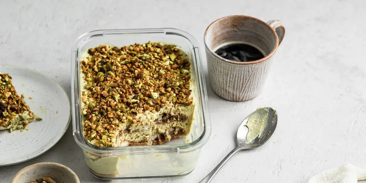 Un delizioso tiramisù al pistacchio, cosparso di granella verde, pronto per essere gustato con un caffè.