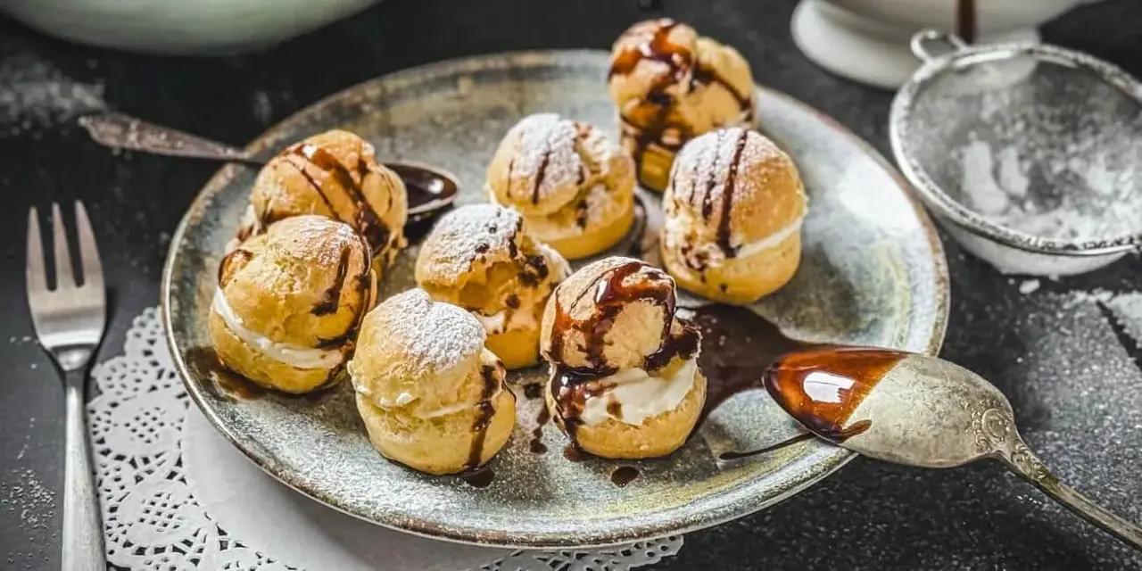 Köstliche Profiteroles, bestäubt mit Puderzucker und beträufelt mit Schokoladensauce. Ein wahrer Genuss, wie beim original profiteroles rezept.