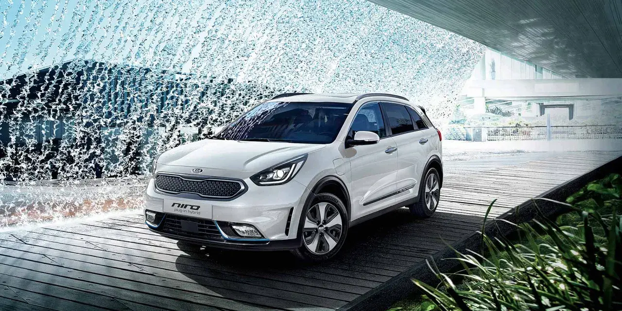 Biały Kia Niro Plug-in Hybrid na drewnianej platformie, otoczony wodnymi kaskadami i zielenią.