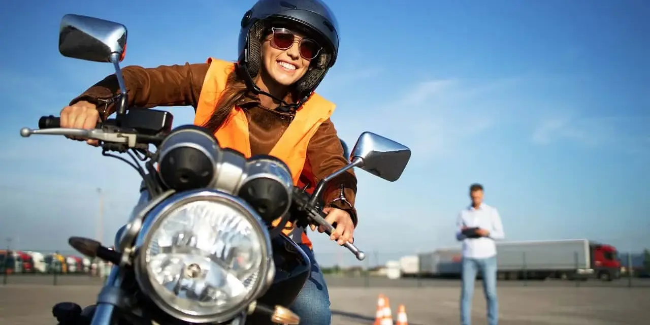 Uśmiechnięta kursantka na motorze, w kasku i kamizelce, uczy się jeździć. Zastanawiasz się, ile kosztuje prawo jazdy na motor?