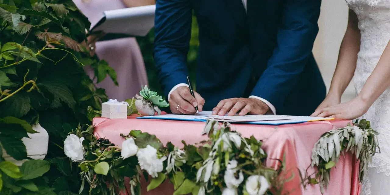 Pan młody podpisuje dokumenty, a obok stoi panna młoda. Zastanawiasz się, ile kosztuje ślub cywilny?