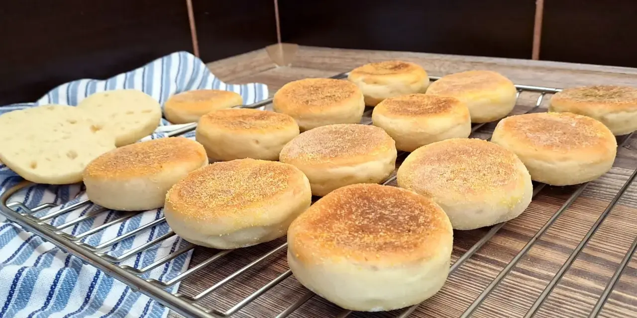Świeżo upieczone muffiny angielskie, lekko zrumienione, czekają na śniadanie. Dwa przekrojone bułeczki odsłaniają puszyste wnętrze.