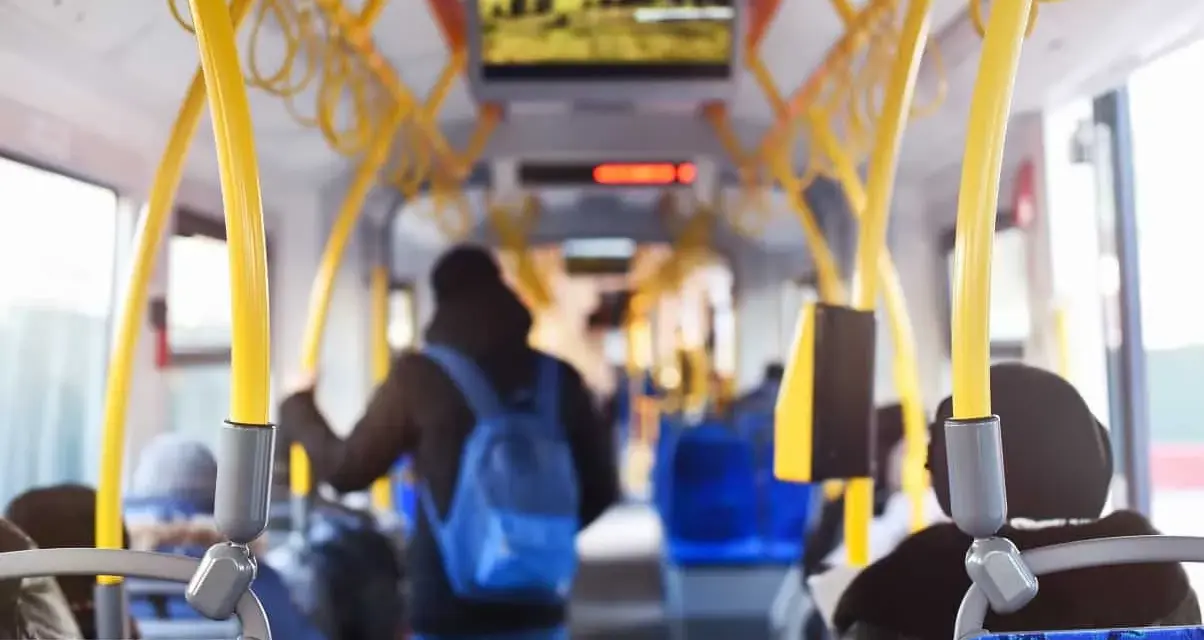 Wnętrze autobusu z żółtymi poręczami. Młody mężczyzna z niebieskim plecakiem idzie do tyłu. Uważaj, by nie dostać mandatu za brak biletu.
