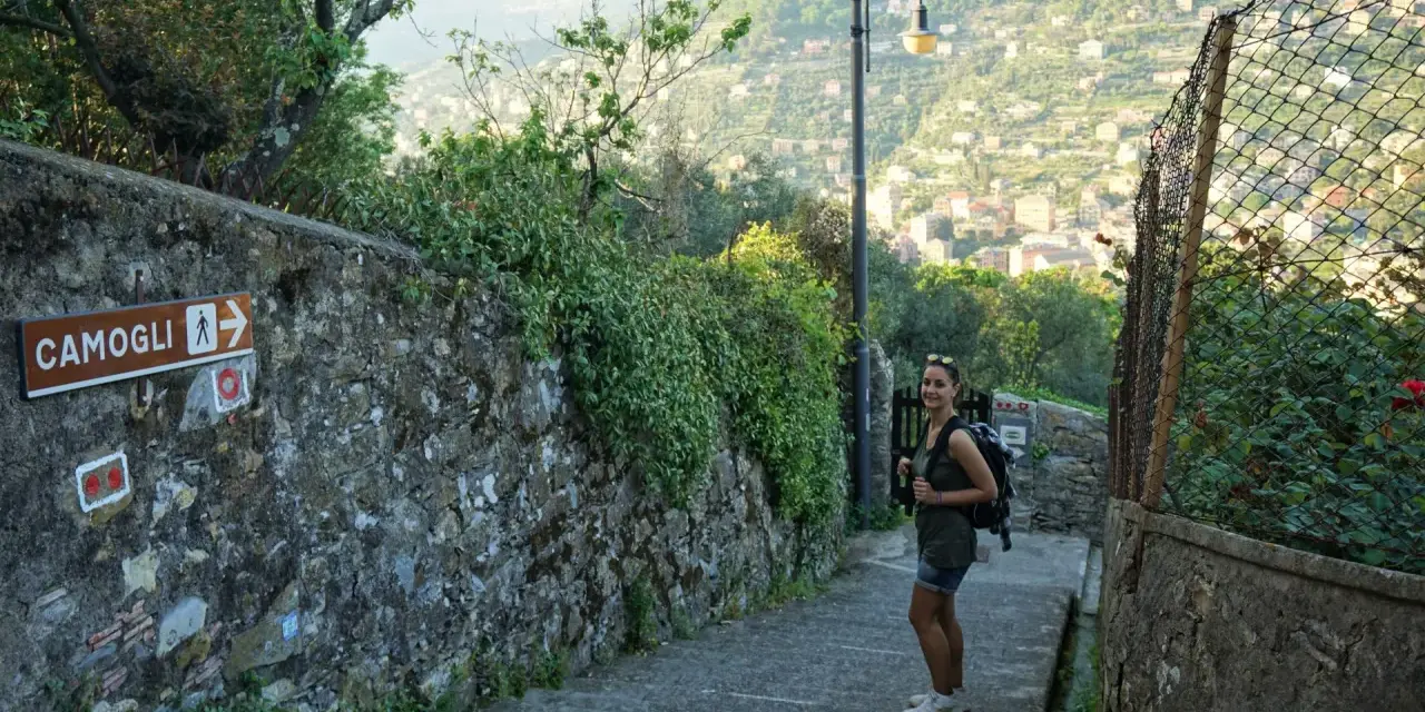 Una ragazza con zaino su un sentiero panoramico, con un cartello che indica Camogli. Perfetto per chi cerca dove dormire sul Cammino del Tigullio.