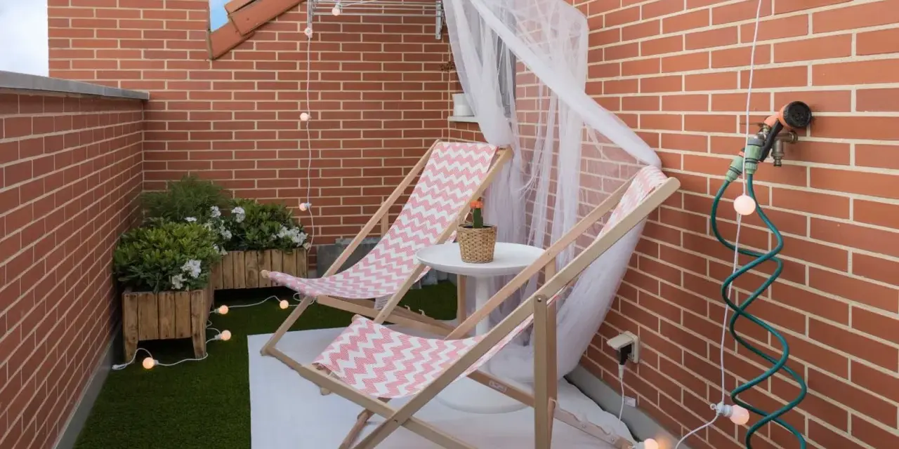 Acogedora terraza de 10 metros cuadrados con dos tumbonas, plantas y luces decorativas. Ideal para relajarse.