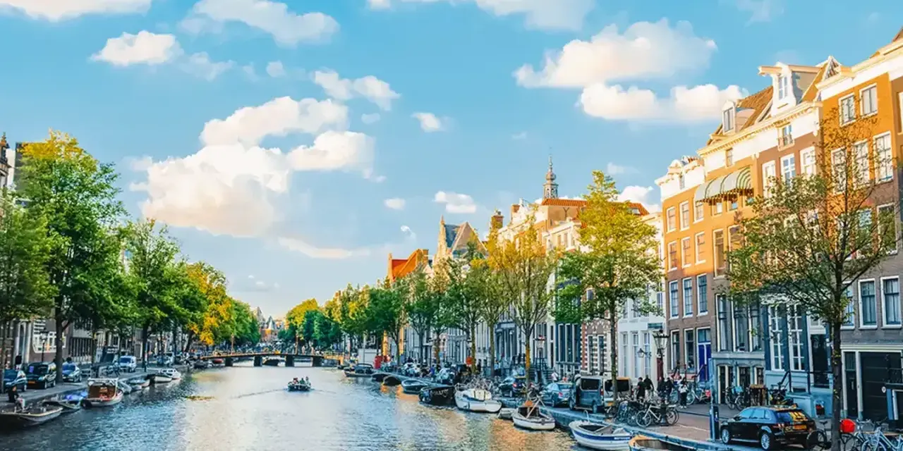 Widok na kanał w Amsterdamie, z łodziami, kamienicami i zielenią. Idealne miejsce na spacer, gdzie jest Amsterdam.