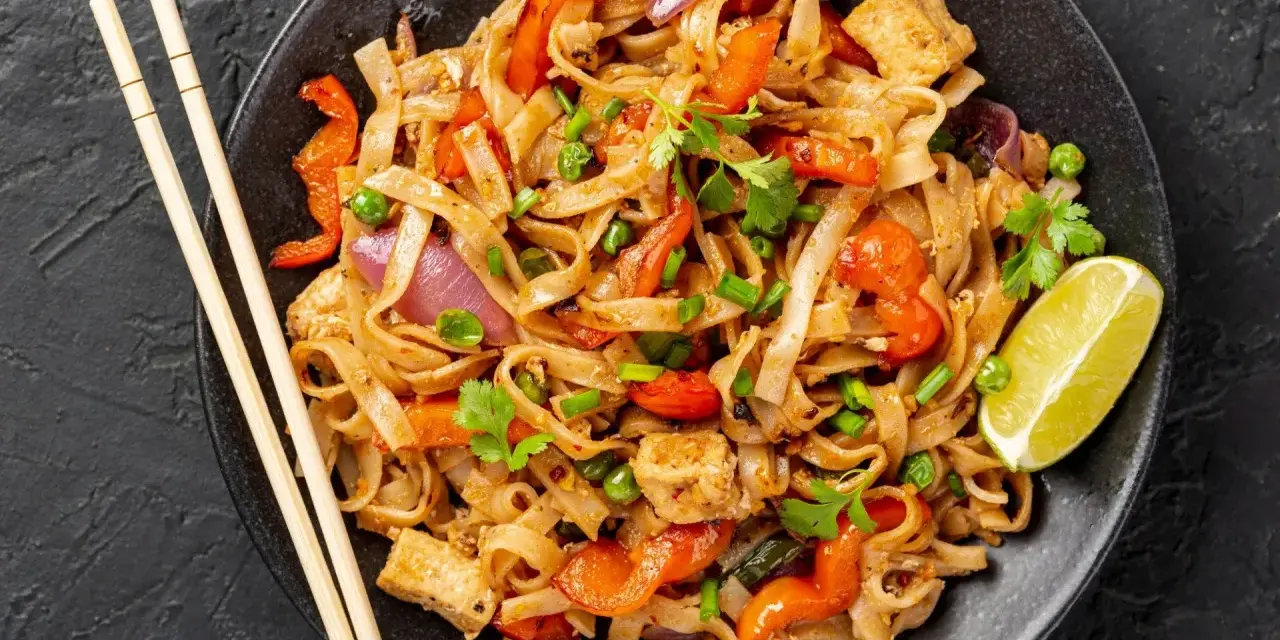 Talerz pełen Pad Thai: makaron ryżowy, tofu, papryka, cebula, groszek i kolendra. Idealny sposób, by dowiedzieć się, pad thai co to.