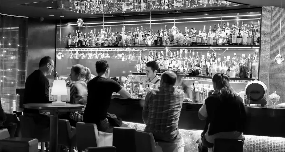 Gente en un bar cine, con un camarero sirviendo bebidas detrás de la barra llena de botellas.
