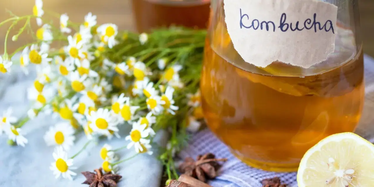 Bouteille de kombucha ambré, décorée de camomille, d'anis étoilé, de bâtons de cannelle et d'une tranche de citron.