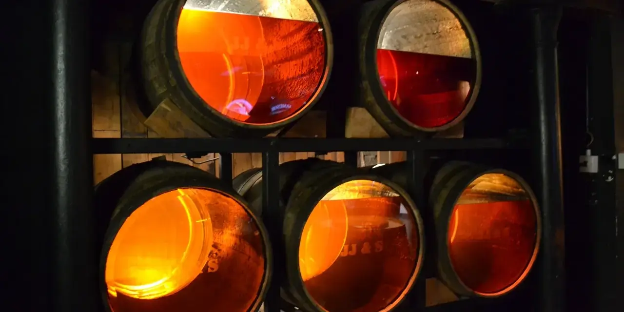 Drewniane beczki z bursztynowym whisky, część trunku to whisky angel share, dojrzewająca w ciemnej piwnicy.
