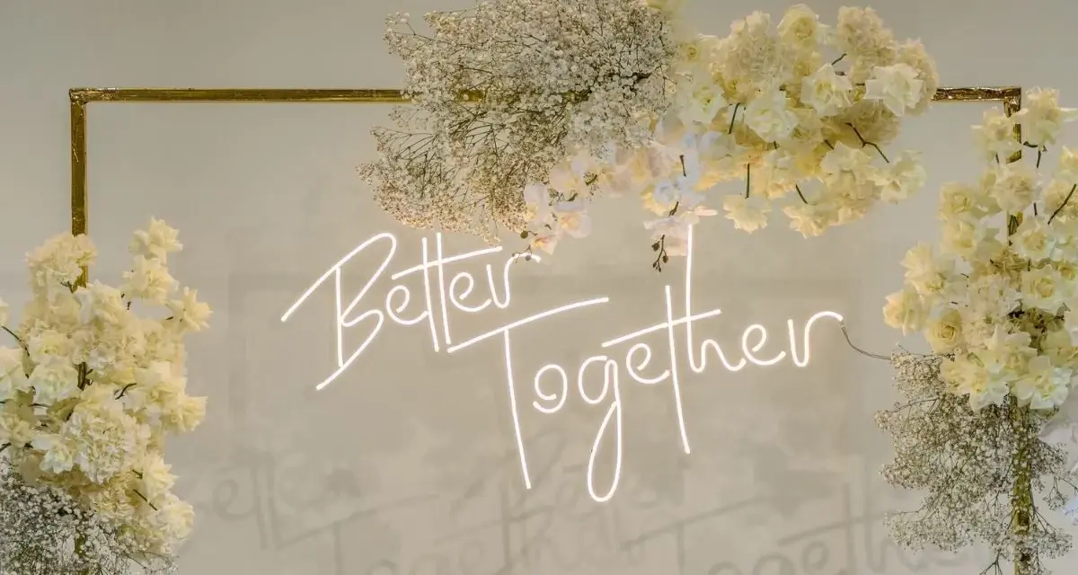 Elegancka ściana z kwiatów w kremowych odcieniach, ozdobiona neonowym napisem "Better Together".