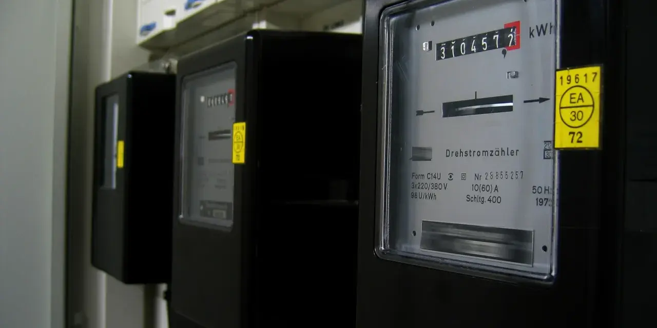 Szereg liczników energii elektrycznej, każdy z wyświetlaczem pokazującym zużycie. Jeden z nich ma żółtą naklejkę z napisem "silnik inwerterowy".