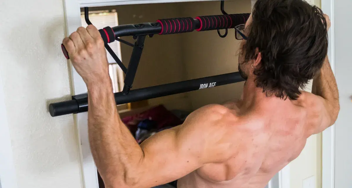 Homme musclé s'entraînant avec une barre de tirage porte d'entrée. Avis : installation facile et solide pour un entraînement efficace.