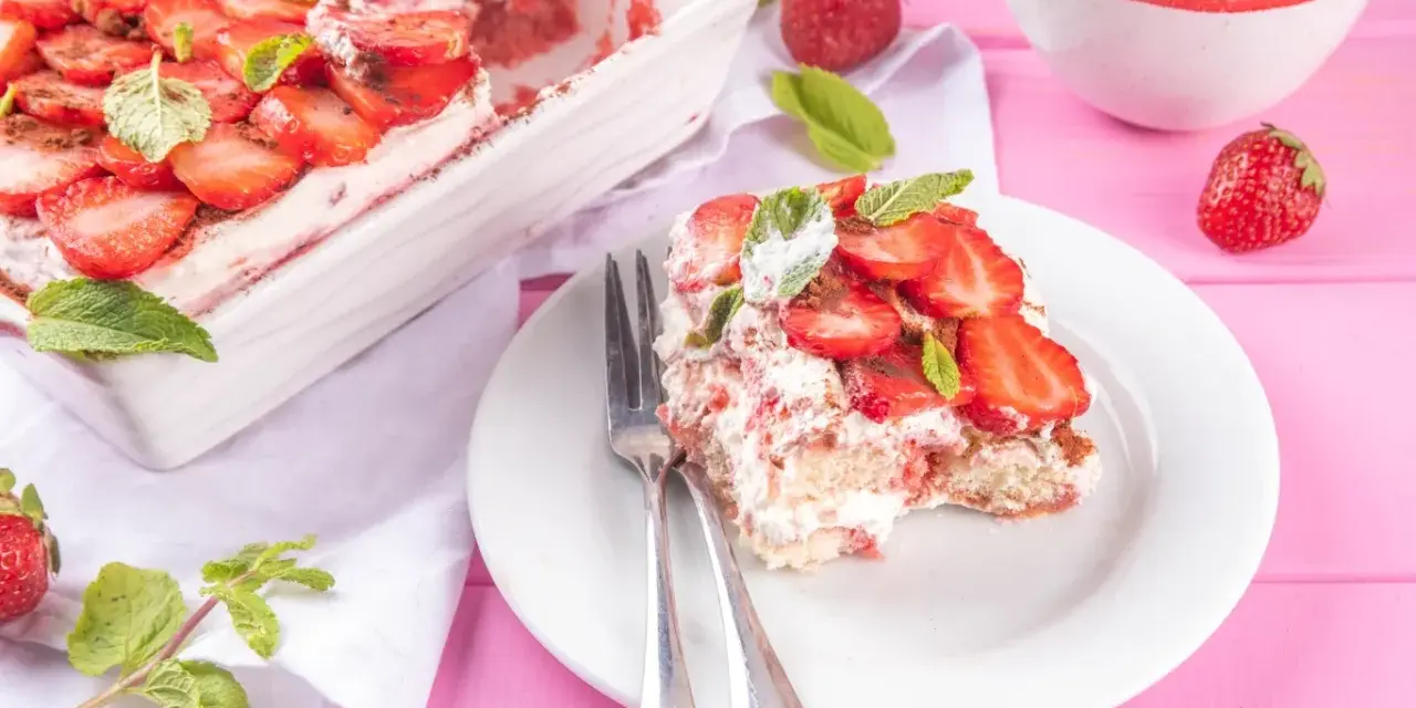 Tiramisu klasyczne kontra tiramisu truskawkowe. Porcja deseru z truskawkami i miętą na talerzu, obok naczynie z deserem i miseczka owoców.