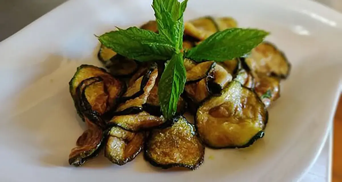 Zucchine alla scapece dorate e croccanti, guarnite con foglie di menta fresca, servite su un piatto bianco.