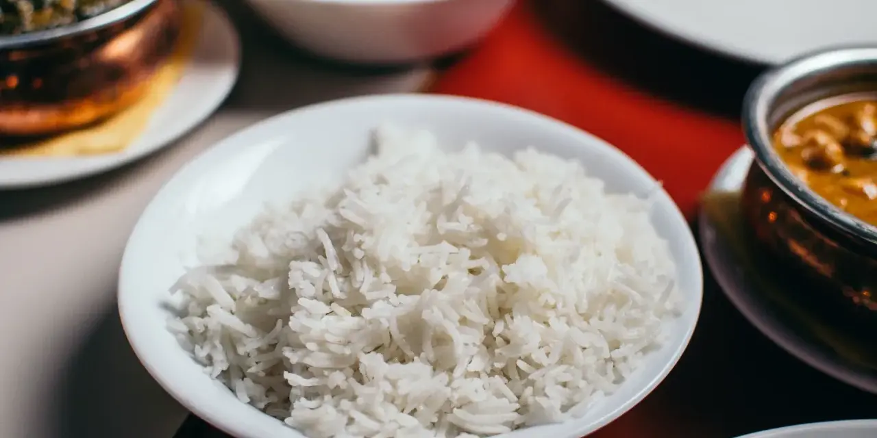 Biały ryż w misce, który jest głównym źródłem węglowodanów w wielu kuchniach. Obok dania curry i sałatka.