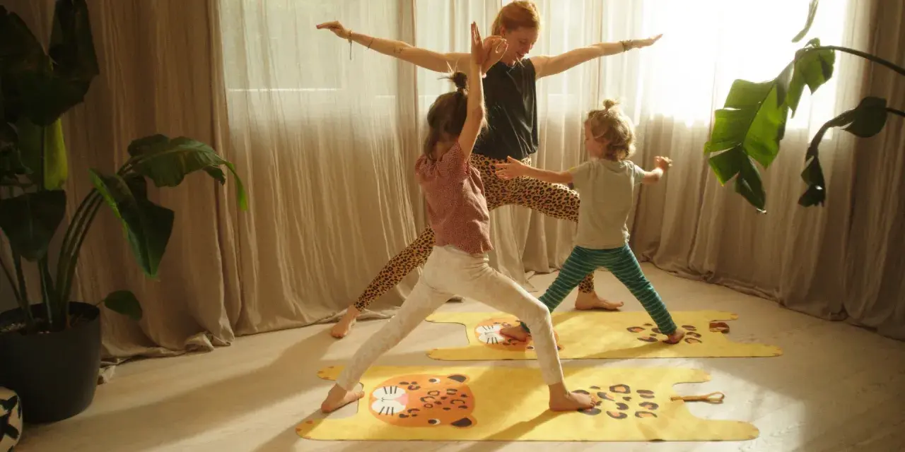 Eine Frau und zwei Kinder üben Yoga auf bunten Matten. Die Kinder haben Spaß bei den Yoga-Übungen.