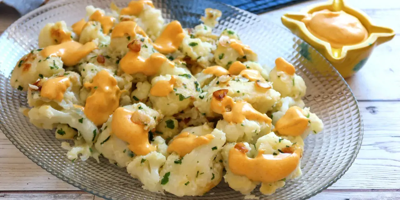 Coliflor al ajillo con salsa cremosa, adornada con perejil fresco y trocitos de ajo crujiente.