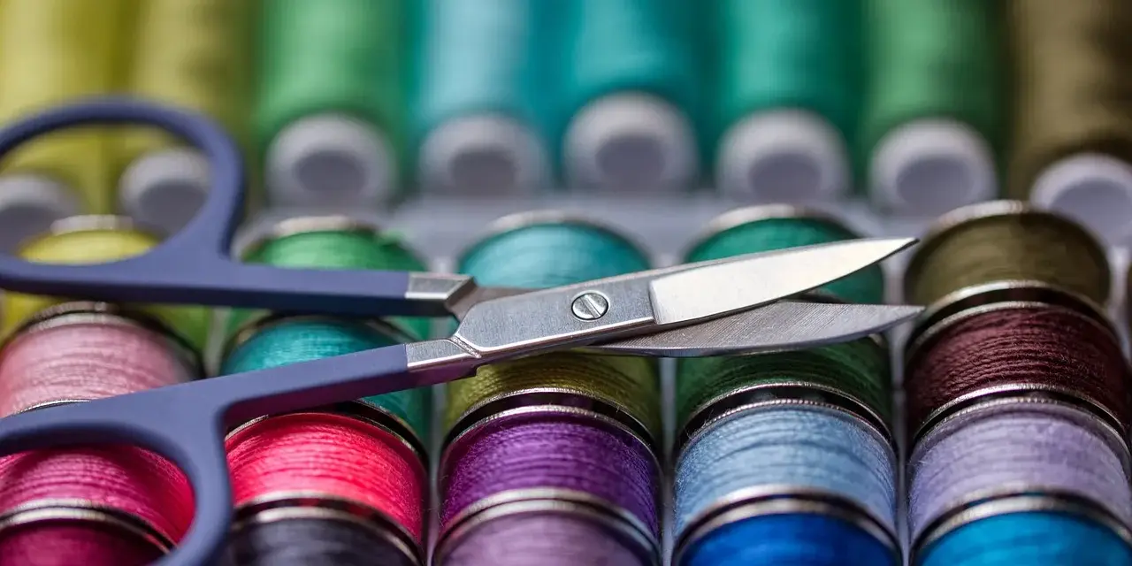 Ciseaux sur une rangée de bobines de fil à coudre aux couleurs vives. Le grosseur de fil à coudre varie, offrant un arc-en-ciel de possibilités créatives.